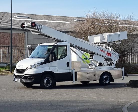 White truck with an extended aerial lift platform parked on a concrete surface near an industrial building.