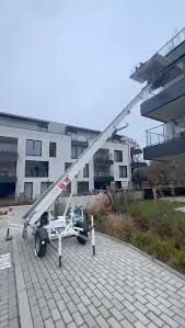 Moving lift positioned against residential building balconies on a paved walkway.